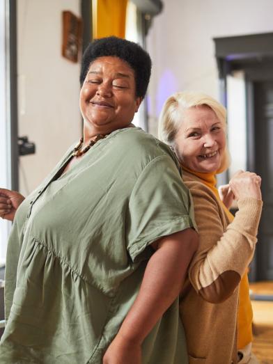 Two women dancing together, one is fighting obesity but having fun